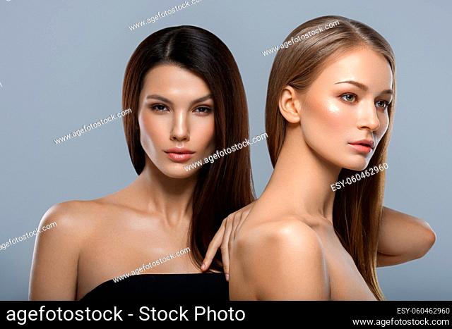 two beautiful young women with natural glowing makeup and long straight hair. beauty shot on gray background. copy space
