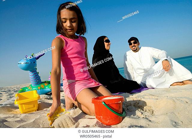 Girl playing in sand while parent sitting behind