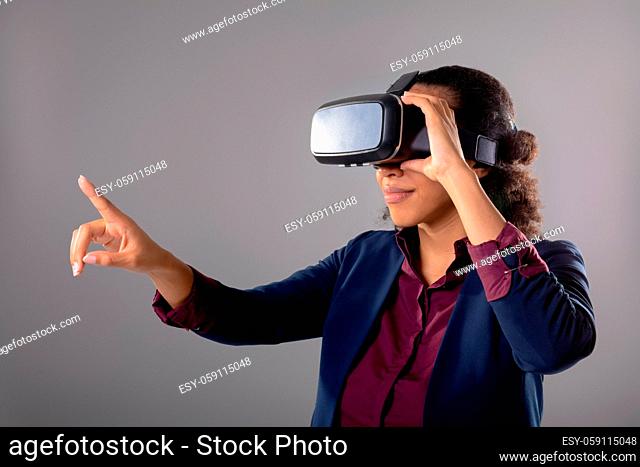 Mid section of businesswoman wearing vr headset touching invisible screen against grey background