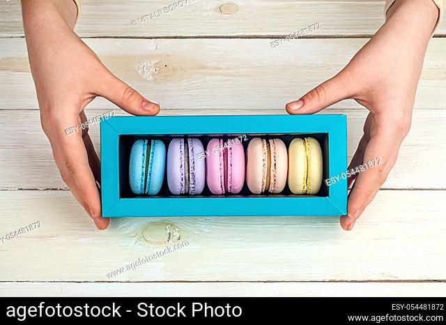 Girl's hands holding box of macaroons on wooden background
