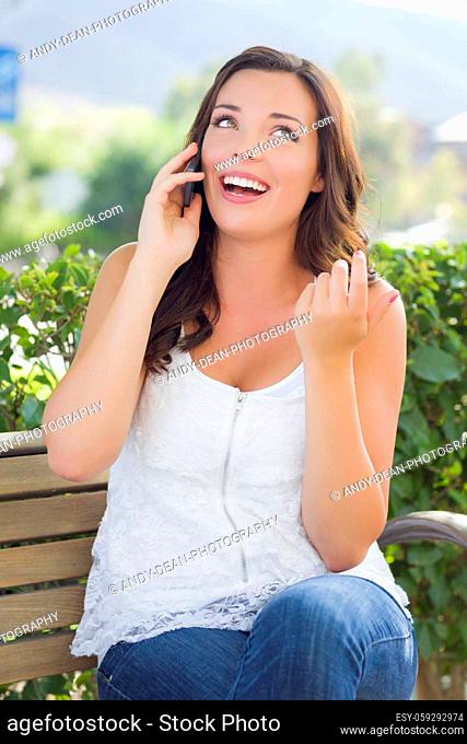Attractive Young Adult Female Talking on Cell Phone Outdoors on Bench