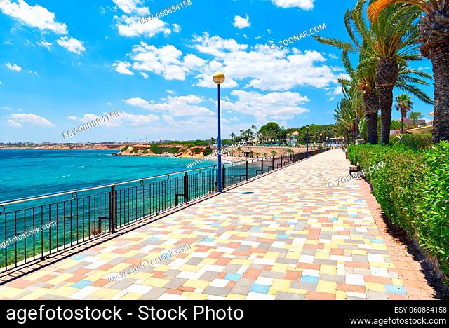Picturesque seafront promenade of Punta Prima. Empty fenced pedestrian walkway and turquoise Mediterranean Sea. Costa Blanca, Spain