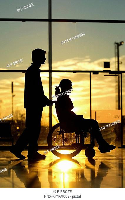 Silhouette of a man pushing a female patient sitting in a wheelchair