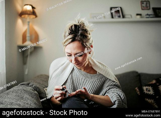 Woman sitting relaxed on the couch, paints her fingernails