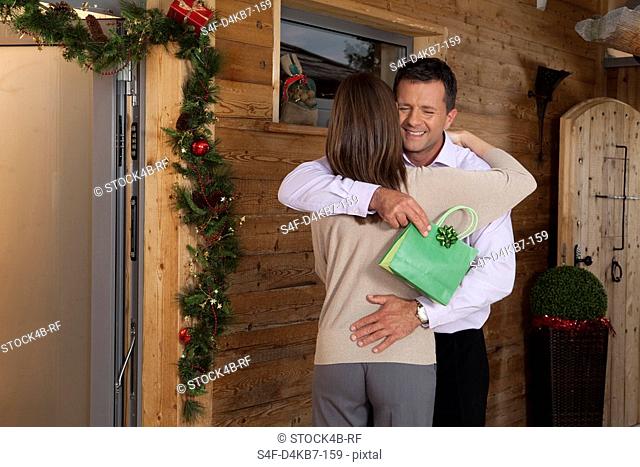 Couple with Christmas present embracing at wooden house