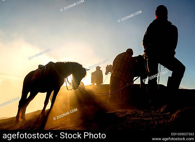 Silhouettes of men and the horses on the top of the hill with misty atmosphere. Mt.Bromo, Indonesia