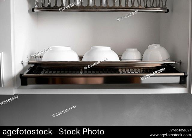 Dish drying metal rack with big nice white clean plates. Traditional comfortable kitchen. Open white dish draining closet with wet dishes of glass and ceramic