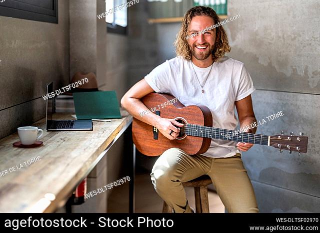 Happy man plucking guitar at home