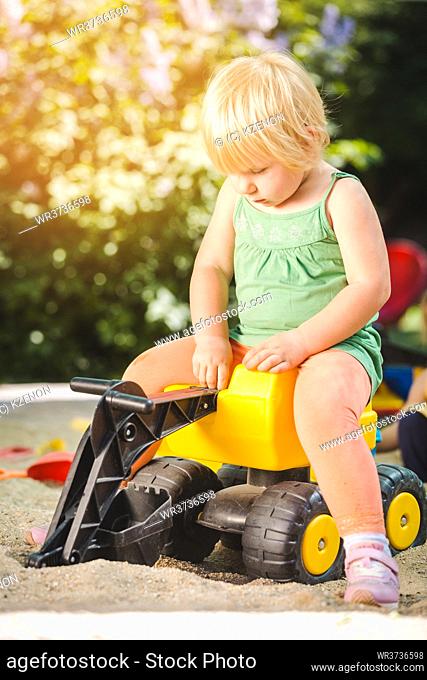 Girl child riding on a yellow toy tractor on playground