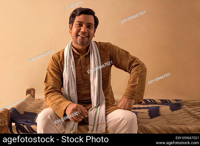 A HAPPY VILLAGER SITTING ON A COT AND SMILING AT CAMERA