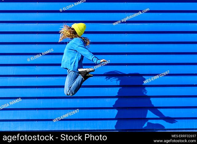 Teenage girl jumping in the air in front of blue background
