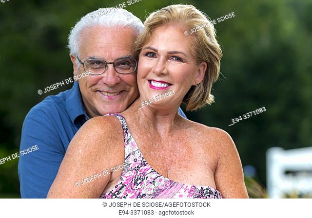 A happy 60 Year old blond woman and a 66 year old man smiling at the camera, outdoors