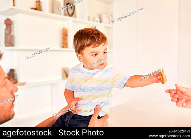 Kleinkind nimmt einen Keks von der Mutter unter Aufsicht von seinem Vater