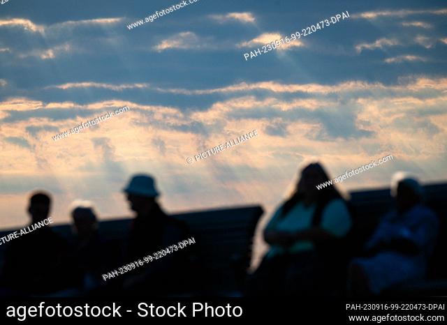16 September 2023, Schleswig-Holstein, Wedel: Sun rays shine through the clouds in front of excursionists on a park bench. Photo: Jonas Walzberg/dpa