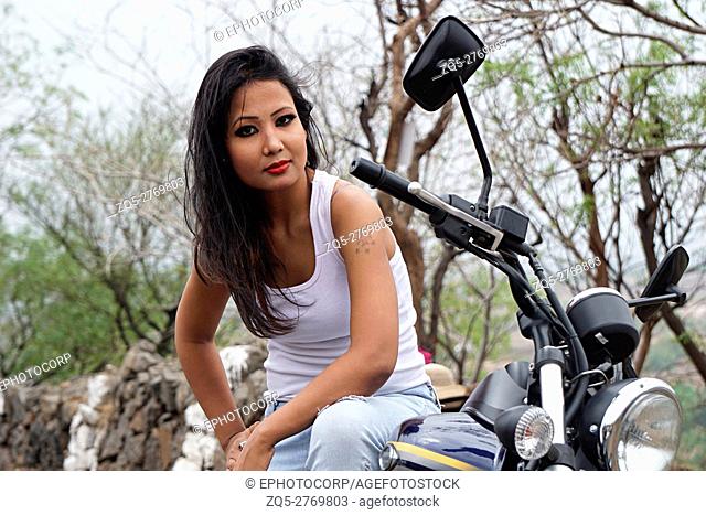 Young woman with tattoo on arm sitting on a motorbike, Pune, Maharashtra