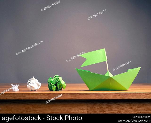 Teamwork business concept with crumpled paper and a paper boat on a wooden office table with space for text, ecology or green ideas concept