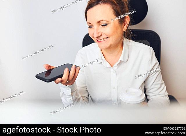 Businesswoman talking on mobile phone using speaker mode. Woman recording audio message using voice assistance and recognition function on smartphone