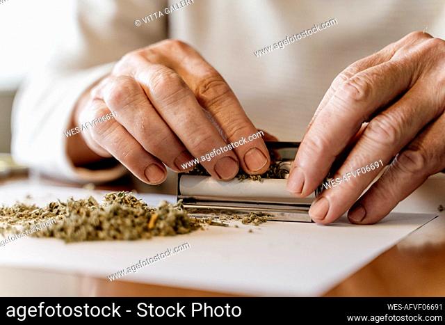 Midsection of retired senior man rolling weed on table