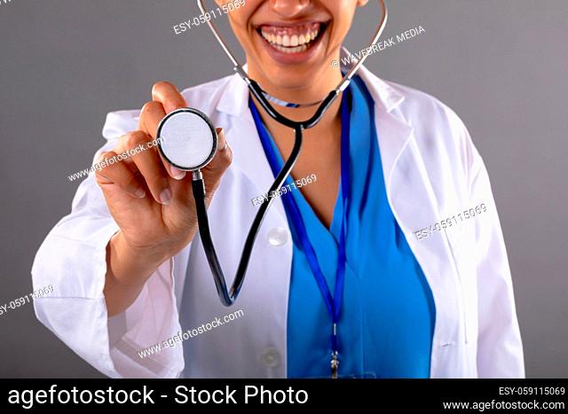 Mid section of african american female doctor holding stethoscope smiling against grey background