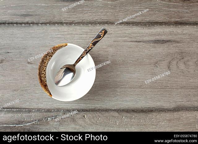Table top view on small empty porcelain bowl with silver decorated spoon, placed on gray wood desk