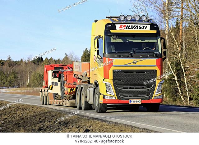 Salo, Finland - March 1, 2019: Yellow Volvo FH truck of Silvasti hauls Sandvik LH209L underground loader or LHD on trailer on highway on day of spring