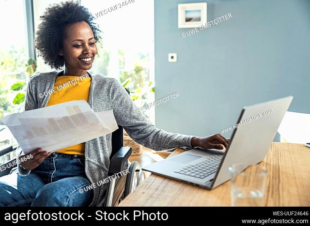Young female freelancer holding document while working on laptop at home office