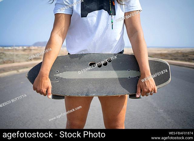 Woman holding skateboard on sunny day