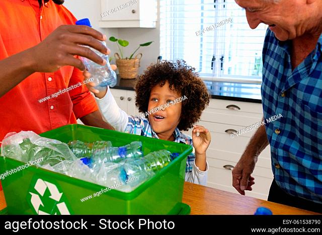 Multiracial father and grandfather teaching boy to recycle waste by throwing plastic bottles in bin