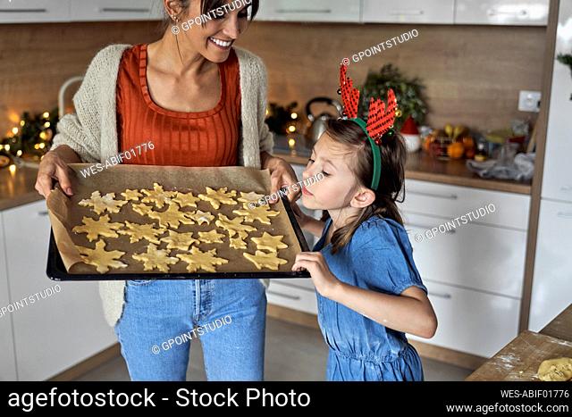 Girl looking at unbaked cookie on pan holding by mother in kitchen