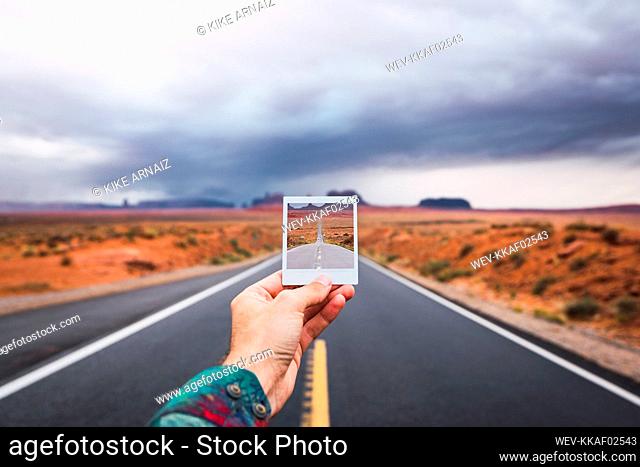 USA, Utah, Hand holding instanf foto over road to Monument Valley