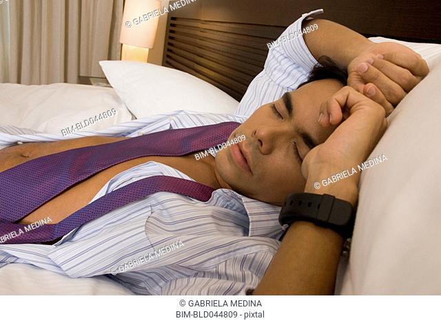 Hispanic businessman sleeping on bed