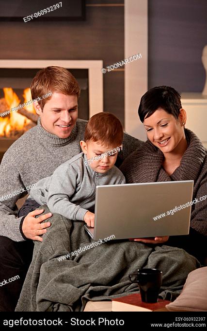 Happy family sitting on couch at home in winter, using laptop computer, smiling