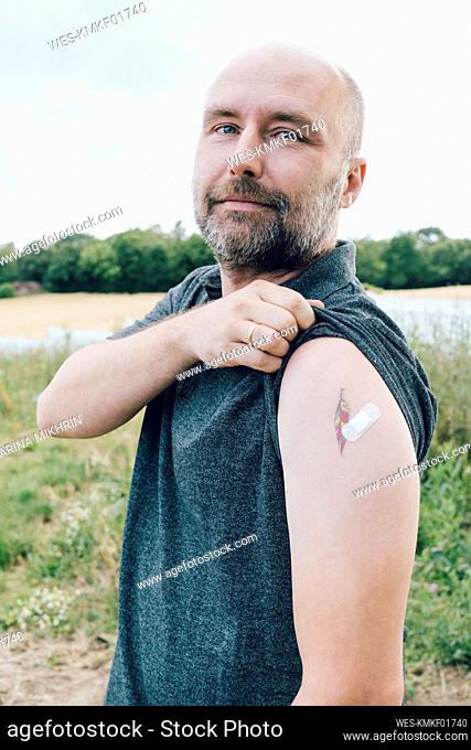 Vaccinated man showing bandage by tattoo on arm