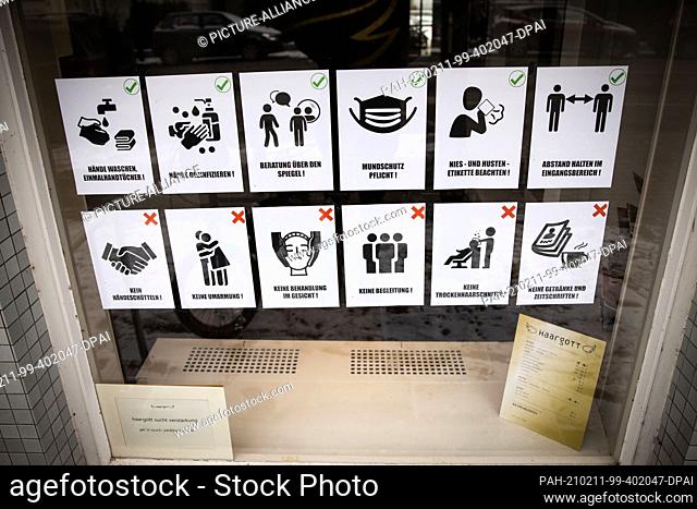 11 February 2021, Hamburg: Notes with pictograms on the rules of conduct due to the Corona pandemic hang in the window of a temporarily closed hairdressing...