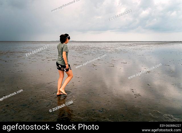 Young woman walking alone in a calm and tranquil beach at low tide in Wadden Sea, Germany. Side view