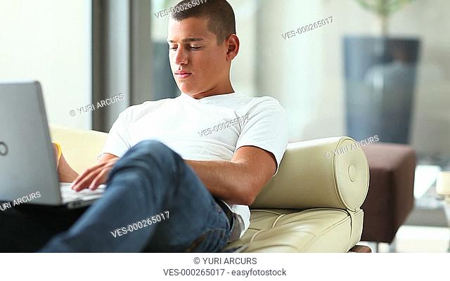 A young man sitting and typing at home on his laptop