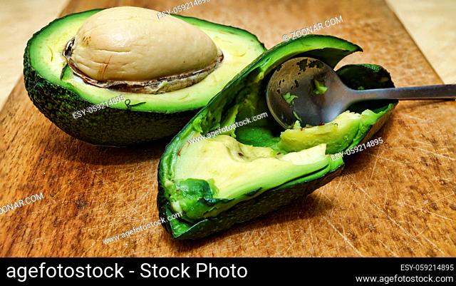 Ripe avocado served for breakfast with a teaspoon on a wooden board. Ripe delicious avocado cut in half on a kitchen board