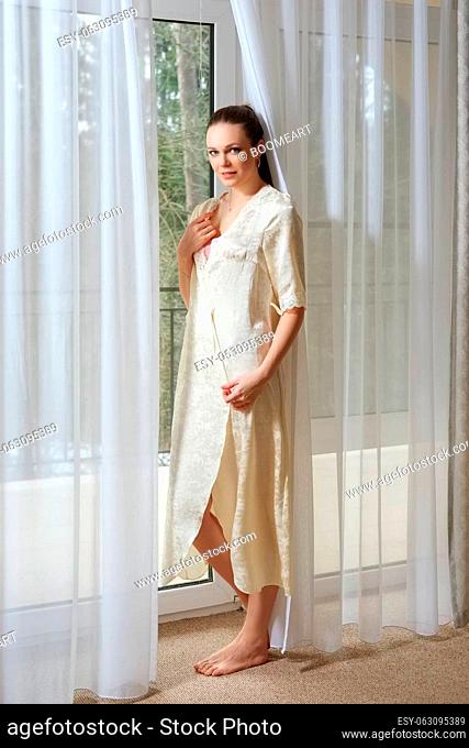 pretty young lady in silk peignoir near the window in bedroom