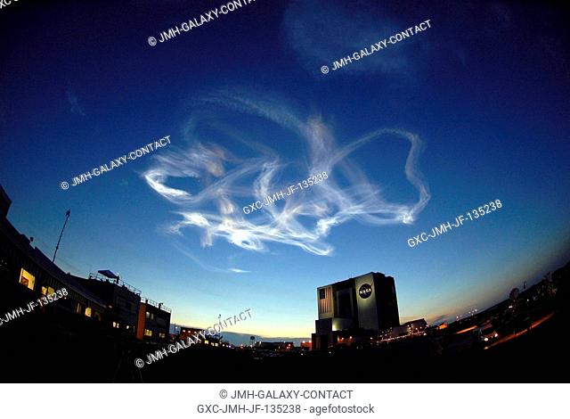 The drifting smoke plumes from the launch of Space Shuttle Atlantis (out of frame) swirl above the Vehicle Assembly Building near sunset