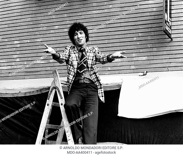 Ninetto Davoli on a ladder. Italian actor Ninetto Davoli gesticulating on a ladder. Behind him, the sign of a tobacconist. Rome, 1970s