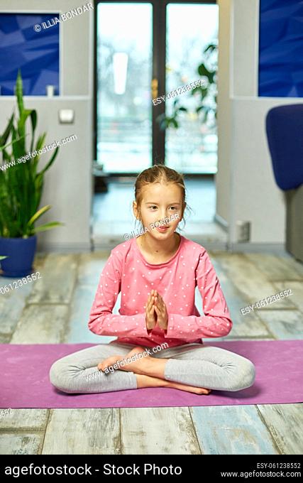 Cute little girl sitting on fitness mat in a Lotus pose with Namaste while doing yoga at home, meditating Playing sports, Healthy lifestyle