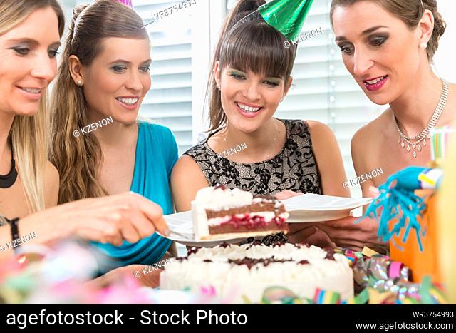 Four beautiful women and best friends smiling while sharing a tasty birthday cake during surprise anniversary at home