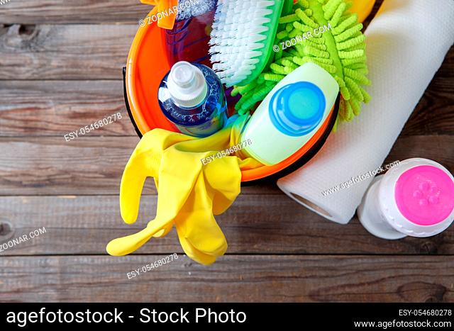 Plastic bucket with cleaning supplies on wood background. Focused on yellow rubber gloves