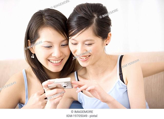 Two young women looking at digital camera, smiling, portrait