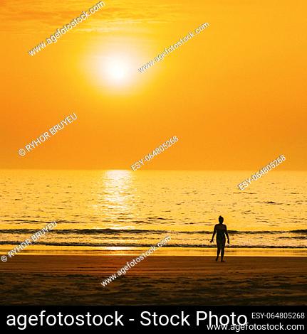 Dark Silhouette Of Young Caucasian Lady Woman In Swimsuit Walking In Sea Beach During Sunset. Vacation On Ocean Beach. Sundown Above Sea Horizon At Sunset