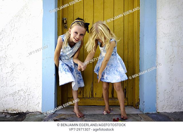 two young candid girls playing and having fun together, outside in front of vintage door. Australian ethnicity