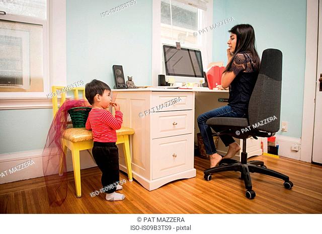 Male toddler eating cookie while mother using laptop