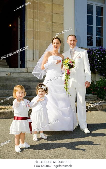 Laughing bride with her groom and their two little daughters in white dresses standing in front of the registrar's