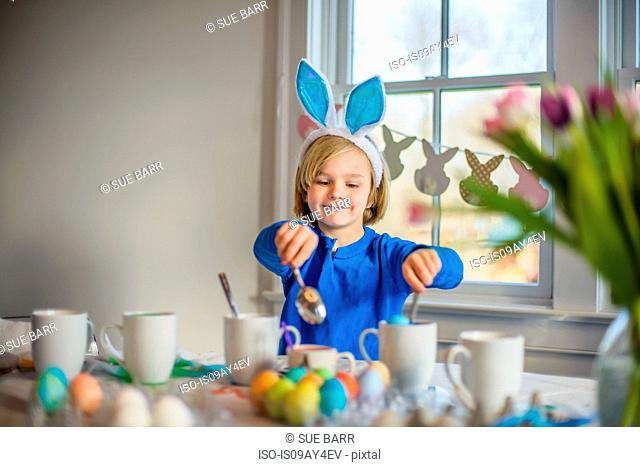 Boy at table wearing bunny ears decorating eggs for Easter