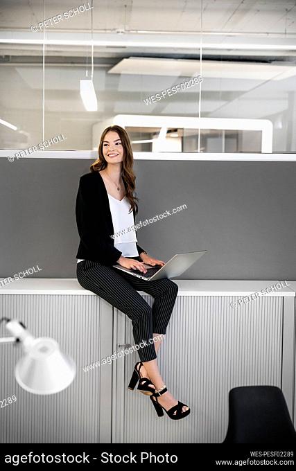 Businesswoman with laptop looking away while sitting on table at office